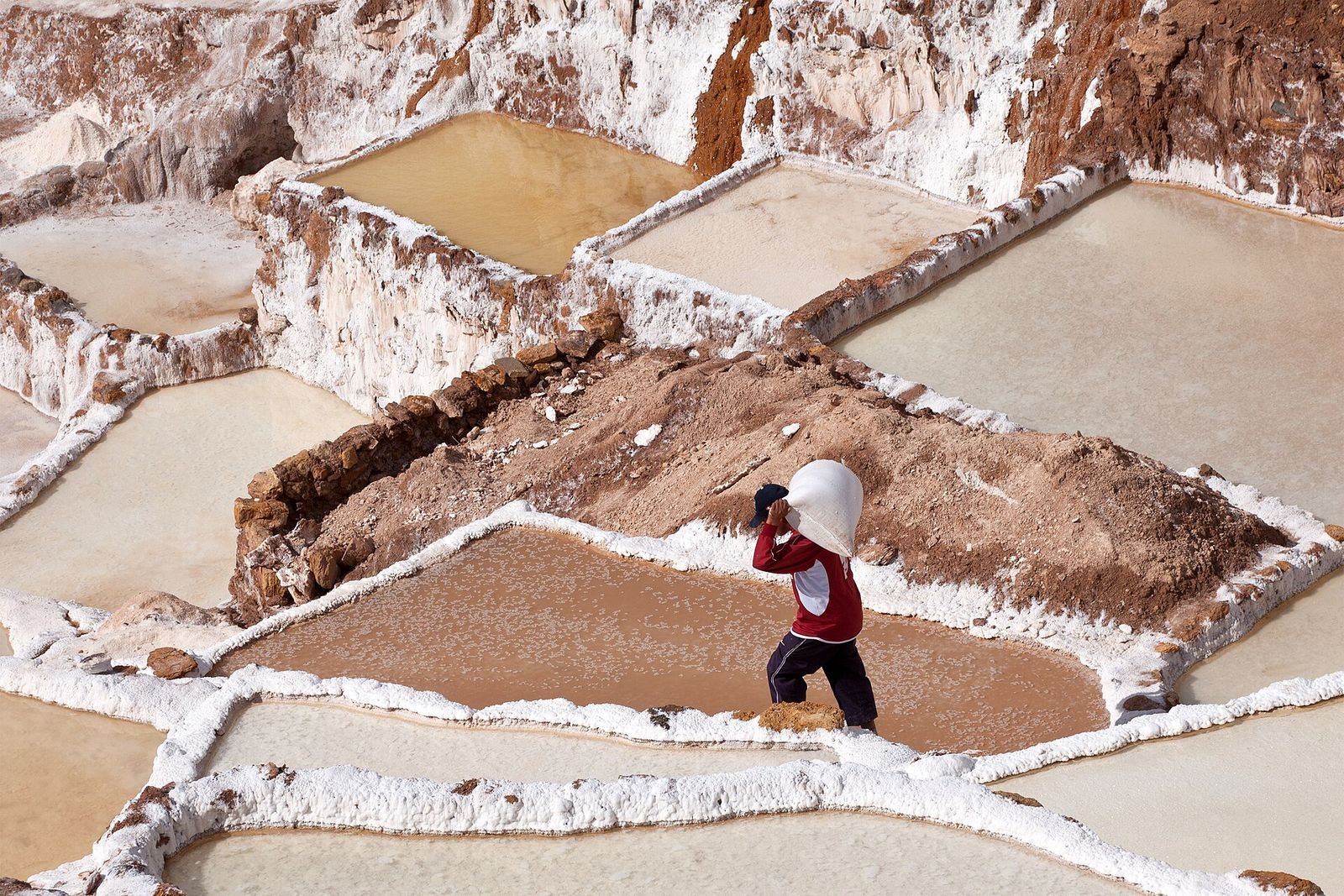 A salt worker carrying a full sack along the edge of the pools
